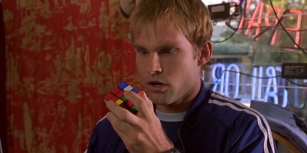 Screencap of Chester, who found a Rubik's cube in the pocket of his blue jogging suit. He is looking numb at it in a cloathing sture.