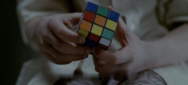 Screencap of Eli who is trying to solve the Rubik's cube. The shot is made of only the hands and the Rubik's cube.