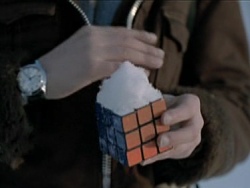 Screencap of Oskar with a solved Rubik's cube in his hand. There is a certain amount of snow on top of the cube, since it is winter.
