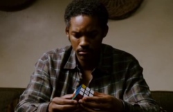Screencap of Chris trying to solve the Rubik's cube, while sitting on the couch. The shot is made van up-front.
