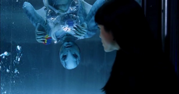 Abe Sapien is floating in an aquarium upside down holding a Rubik's Cube only solved for two sides. A girl named Liz Sherman is sitting in front of the aquarium.